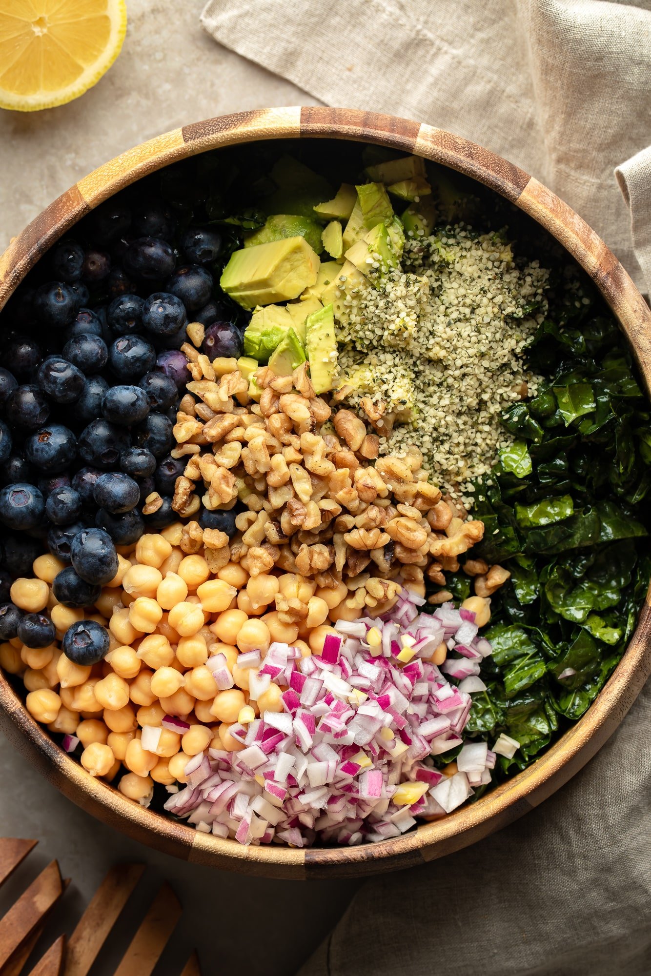 A Kale salad topped with seeds, nuts, beans, vegetables and fruits in a large bowl of salads.