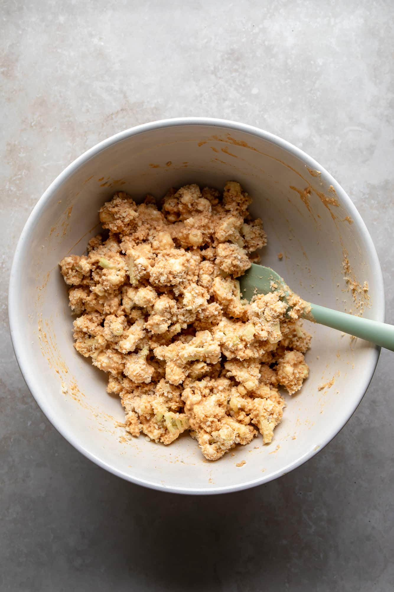 Using a spatula to coat cauliflower flowers in the blender in a white bowl.