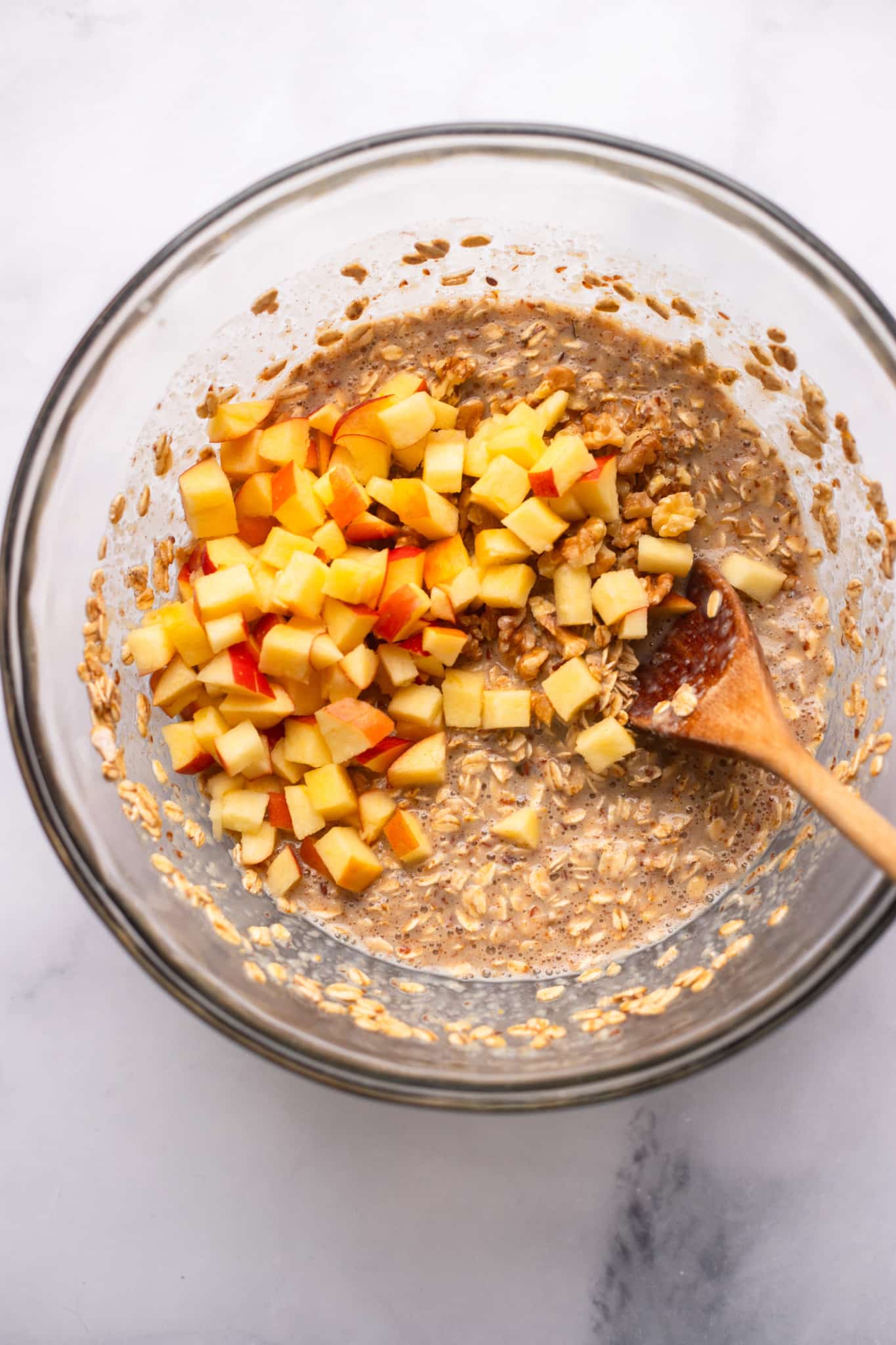 Using a wooden spoon to fold the chopped apples in a oats mix.
