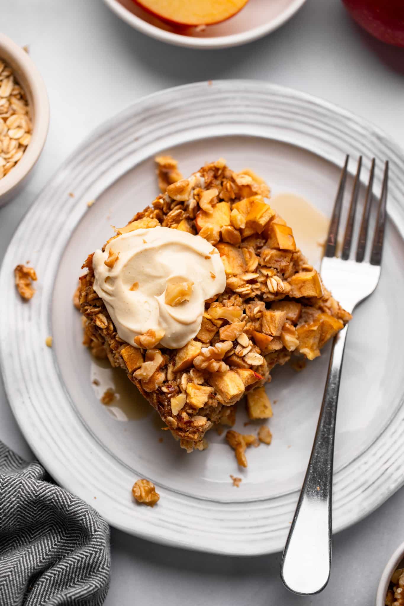 A slice of oatmeal flour in the apple oven with a yogurt dollop on top on a white plate with a fork next to it.