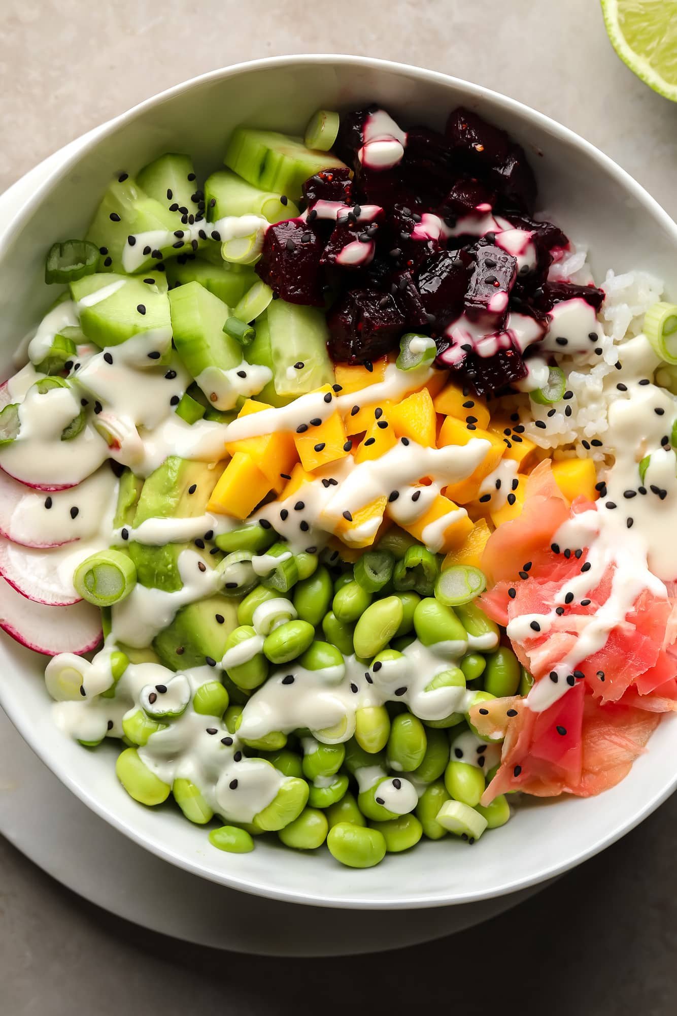 A beet bowl topped with marinated beets, mango, radishes, edamame, cucumber, vinegar ginger and wasabi mayo.