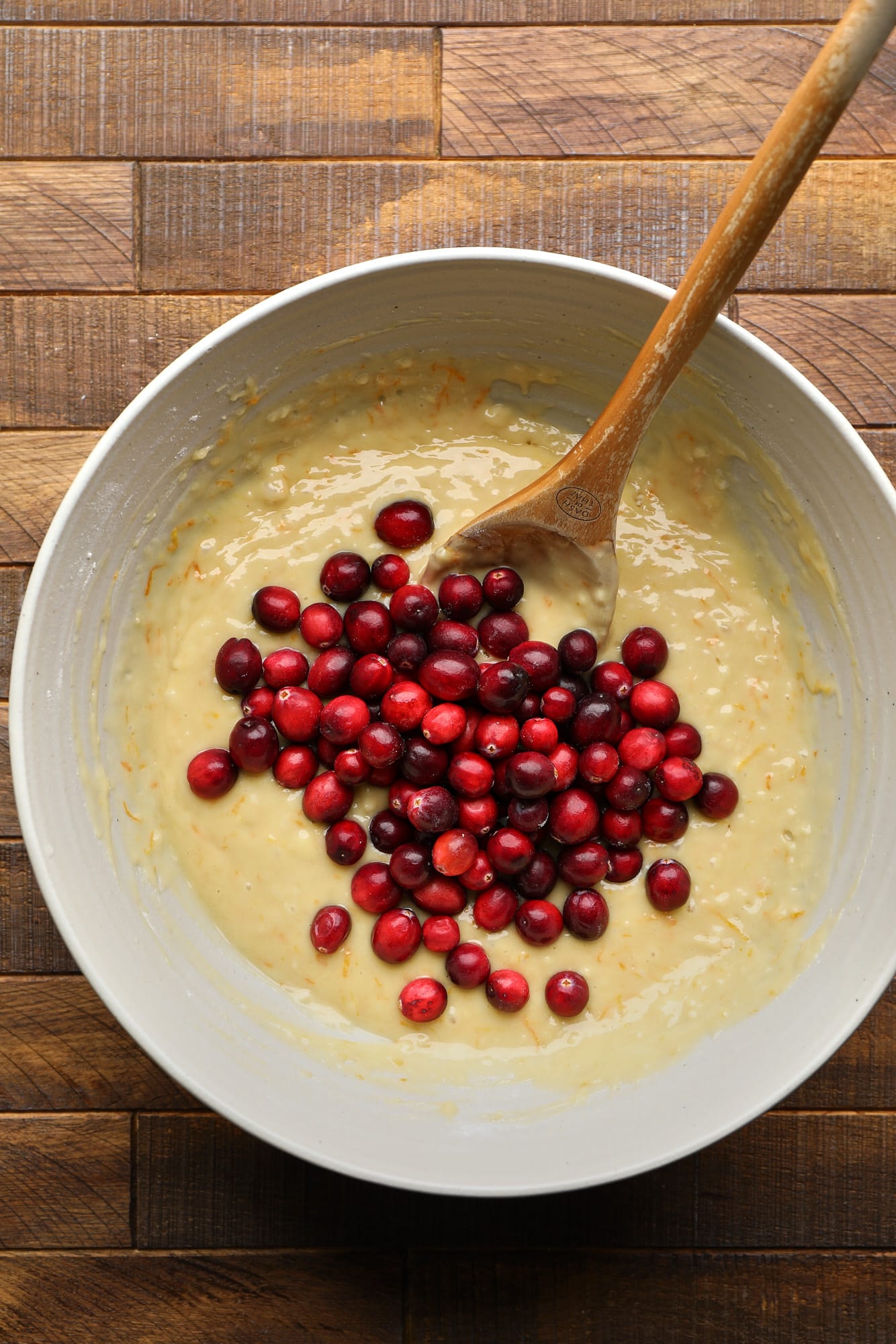 Using a wooden spoon to fold the whole cranberries in cupcake batter.