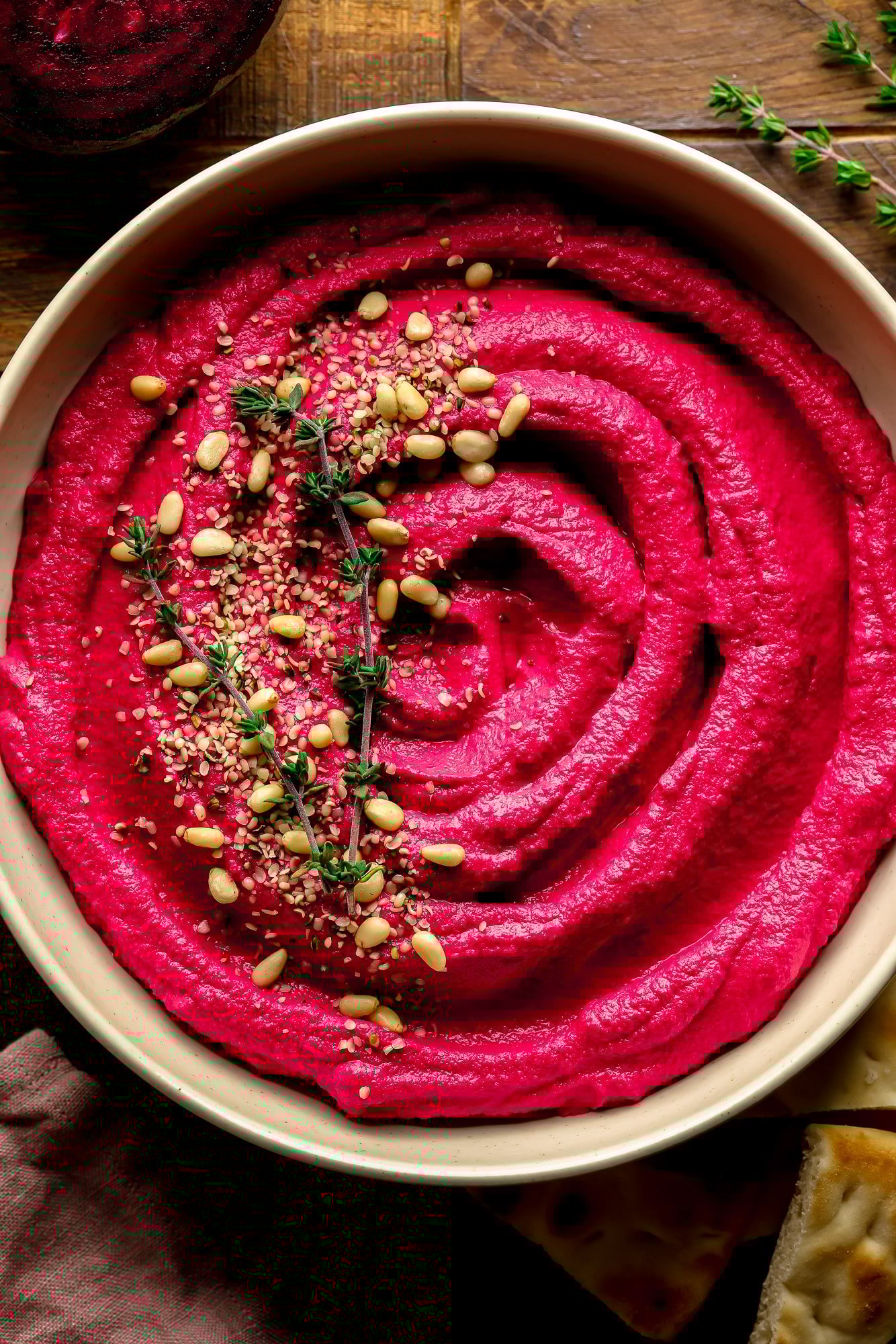 A bowl of pink beets with pine nuts and thyme on top.