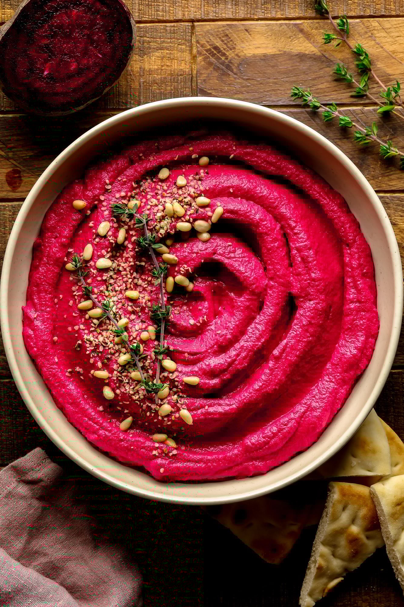 A bowl of pink beets with pine nuts and thyme on top.