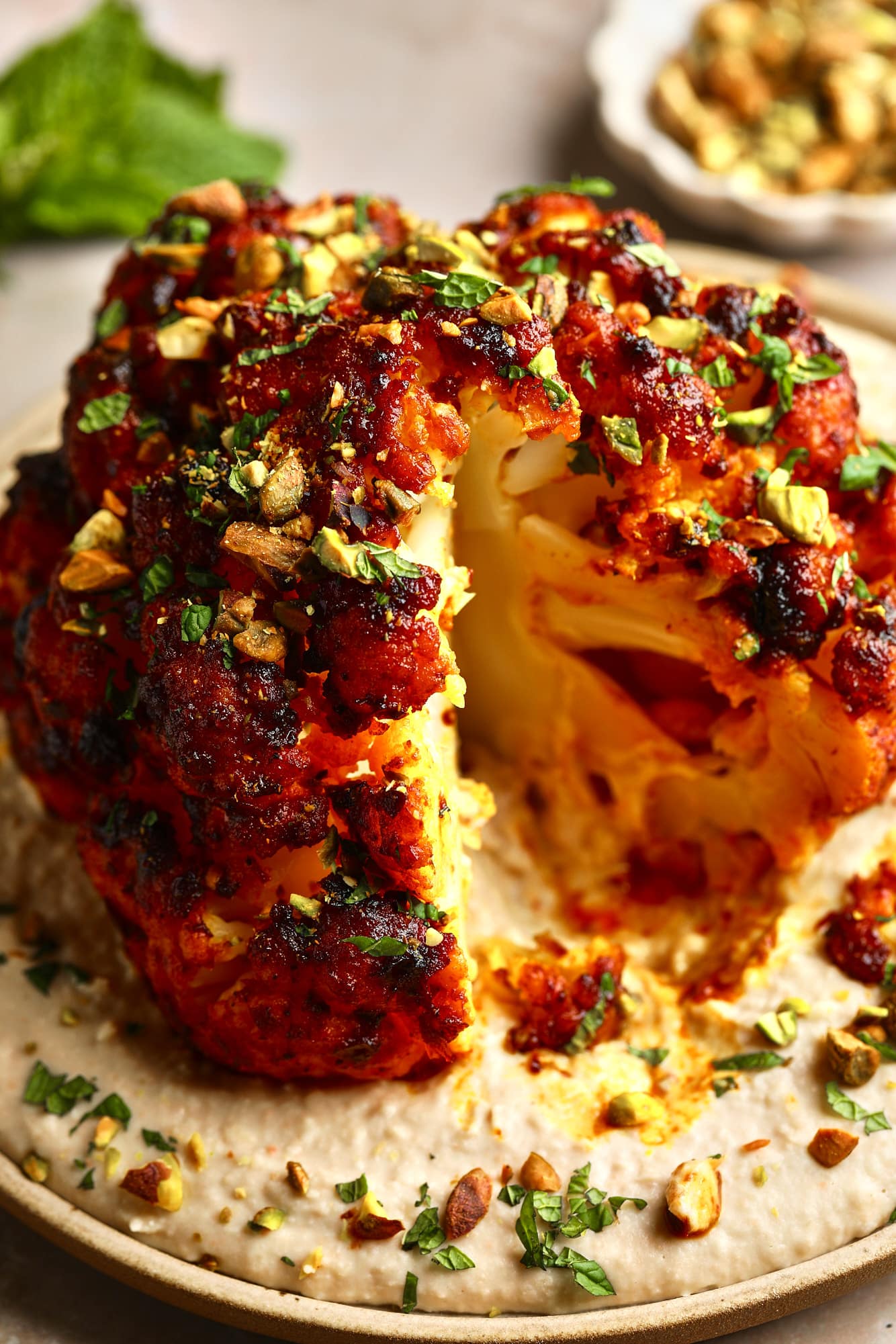 Near a sliced sliced roast cauliflower head on a white bean spread over a plate.