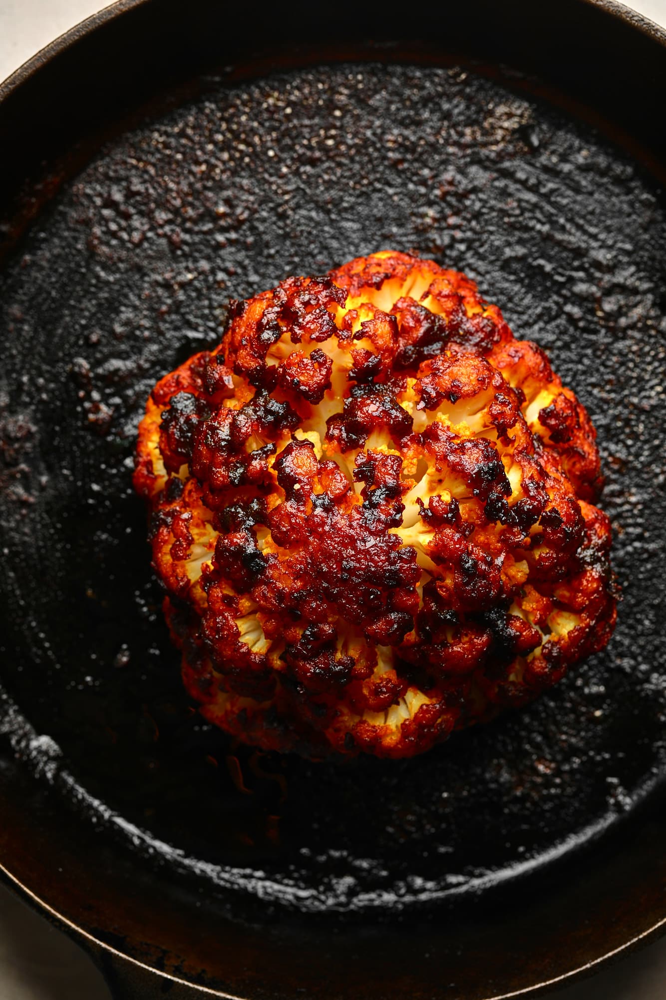A roast cauliflower head with Harissa frost in a black paella.