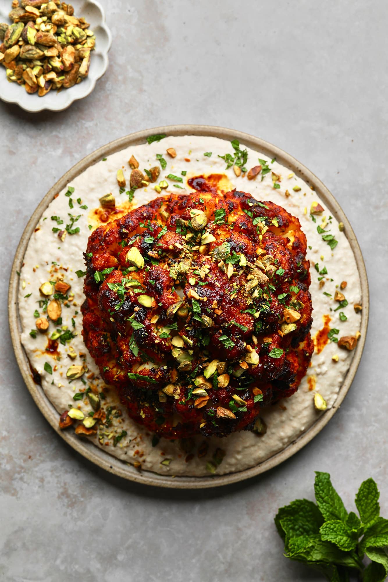 A roast cauliflower head with Harissa frost on a white bean spread over a plate.