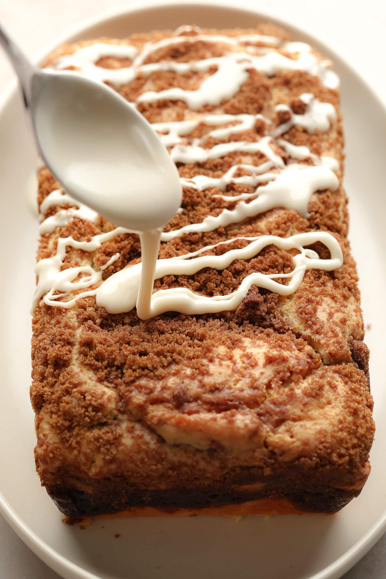 Rashing a white glaze of a spoon on top of a vegan cinnamon bread.