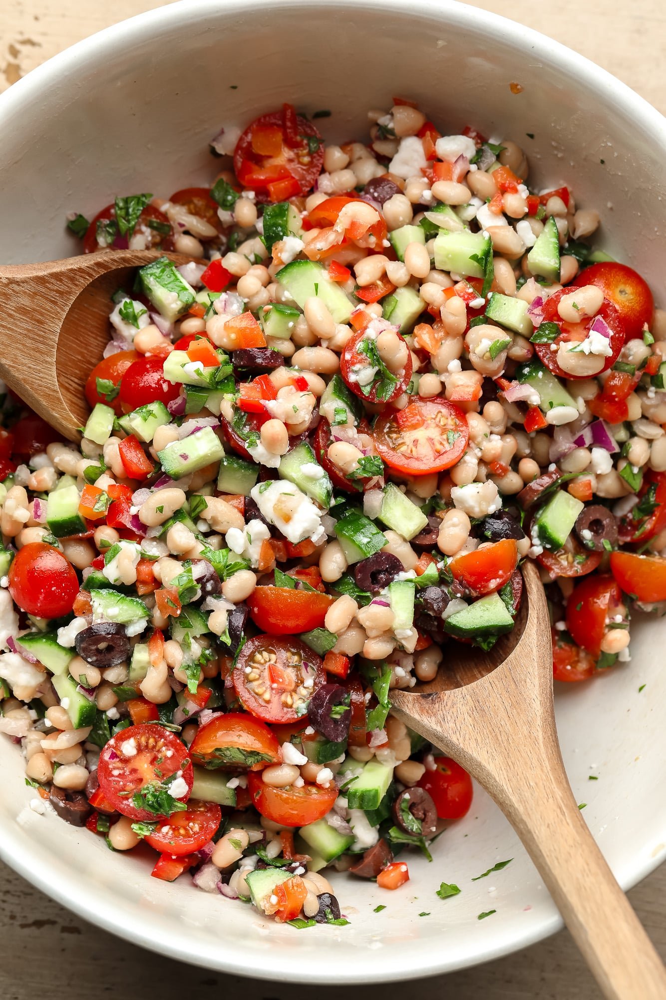 Using two wooden spoons to throw a white beans salad together.