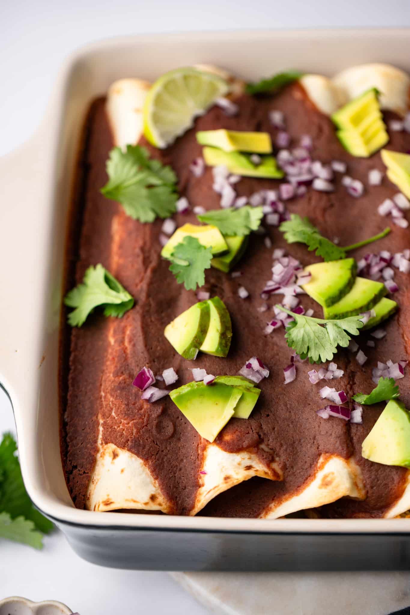 Rocated vegetables with black beans sauce topped with avocado, onion and cilantro on a cooking dish.