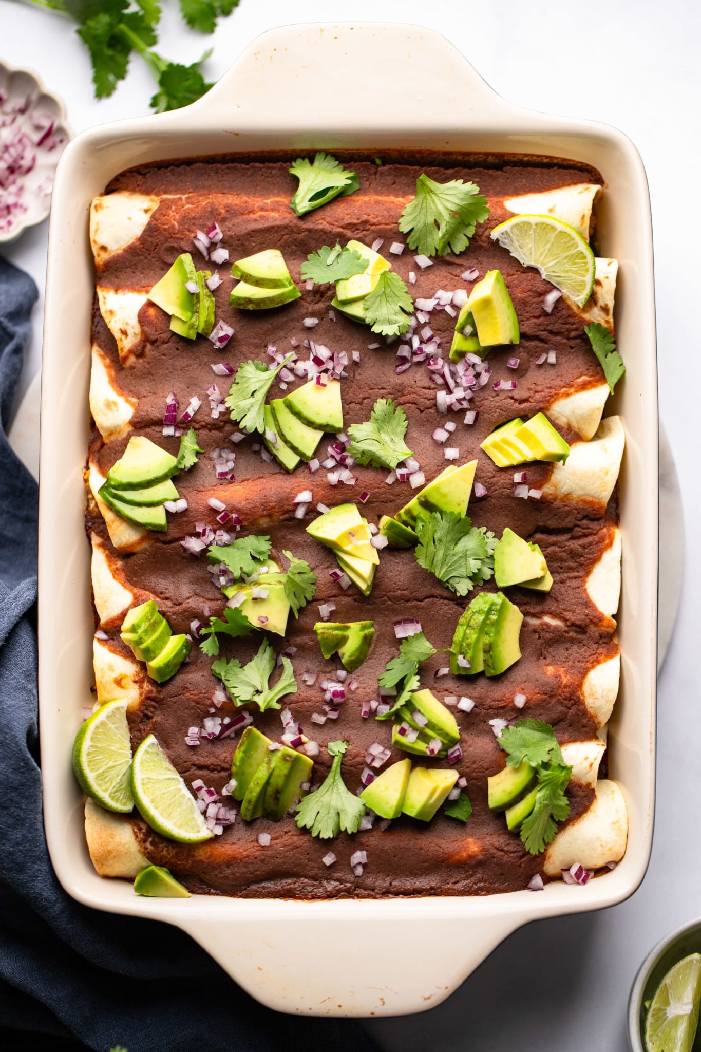 Rocated vegetables with black beans sauce topped with avocado, onion and cilantro on a cooking dish.