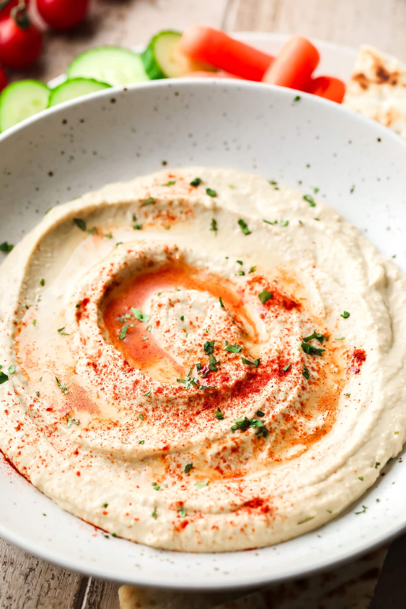 Creamy hummus topped with paprika, herbs and oil in a white bowl.