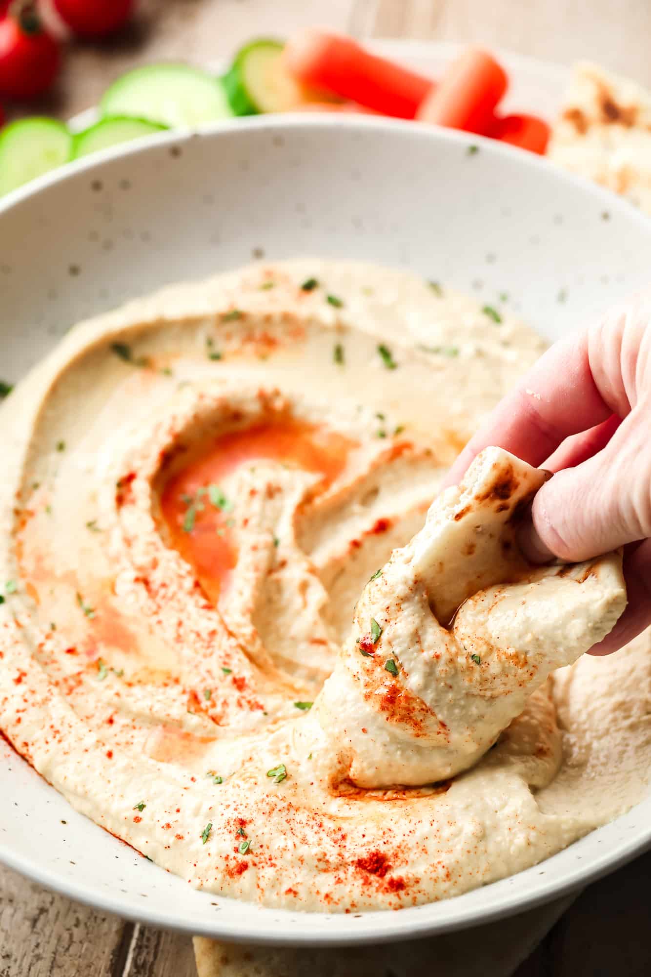 A pita bread in the hand in a bowl of hummus.