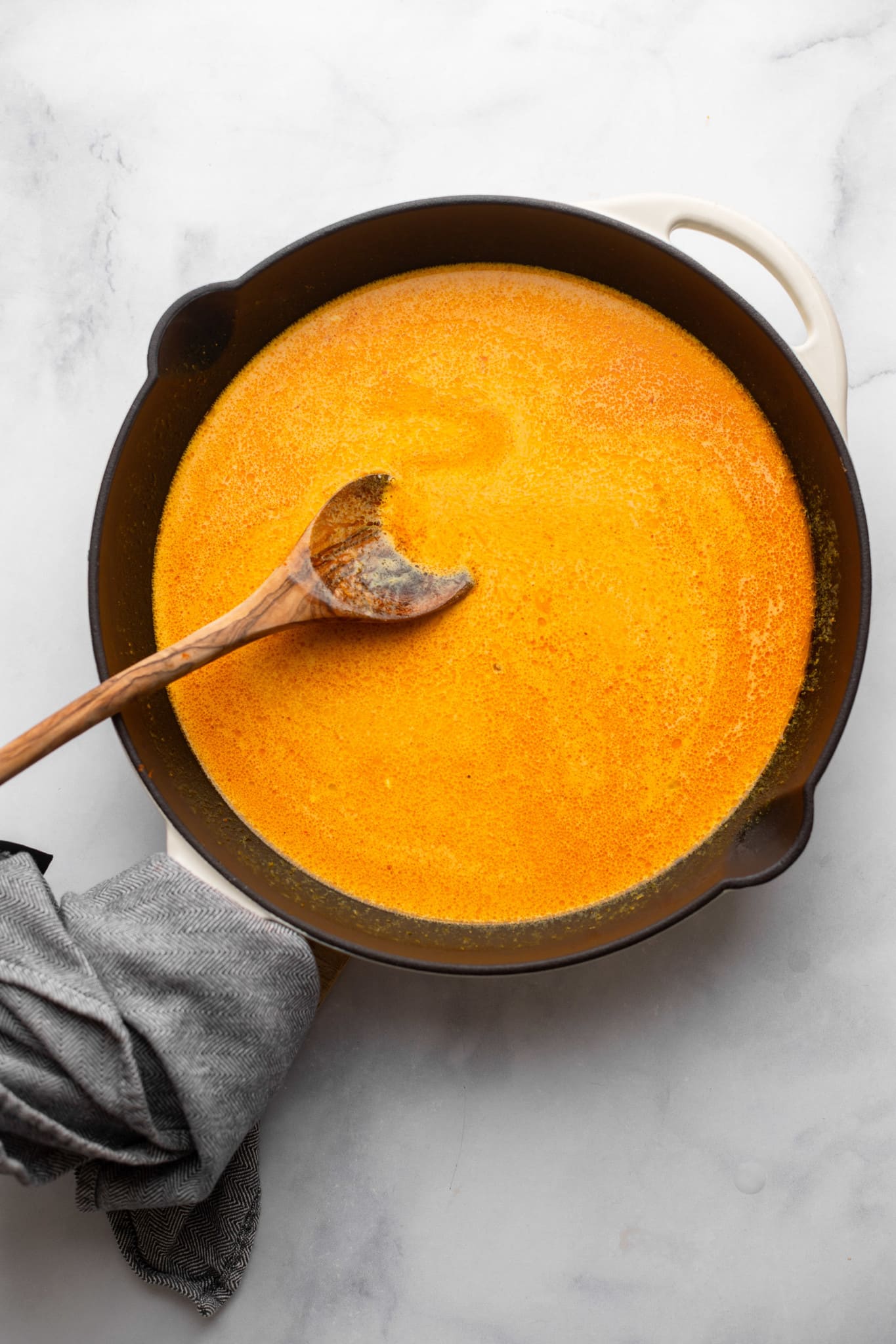 Stirring the red curry sauce with a wooden spoon in a black pan.