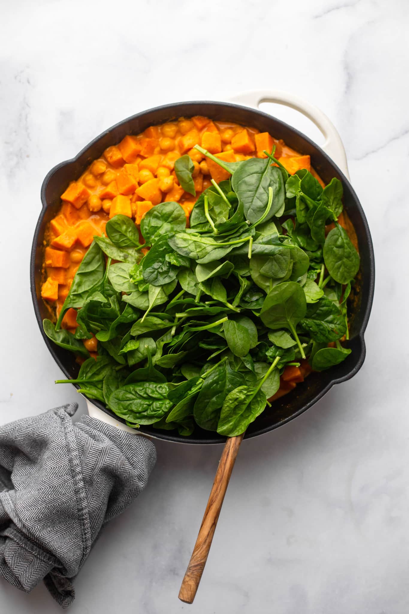 Fresh spinach on the top of the red curry in a black pan.