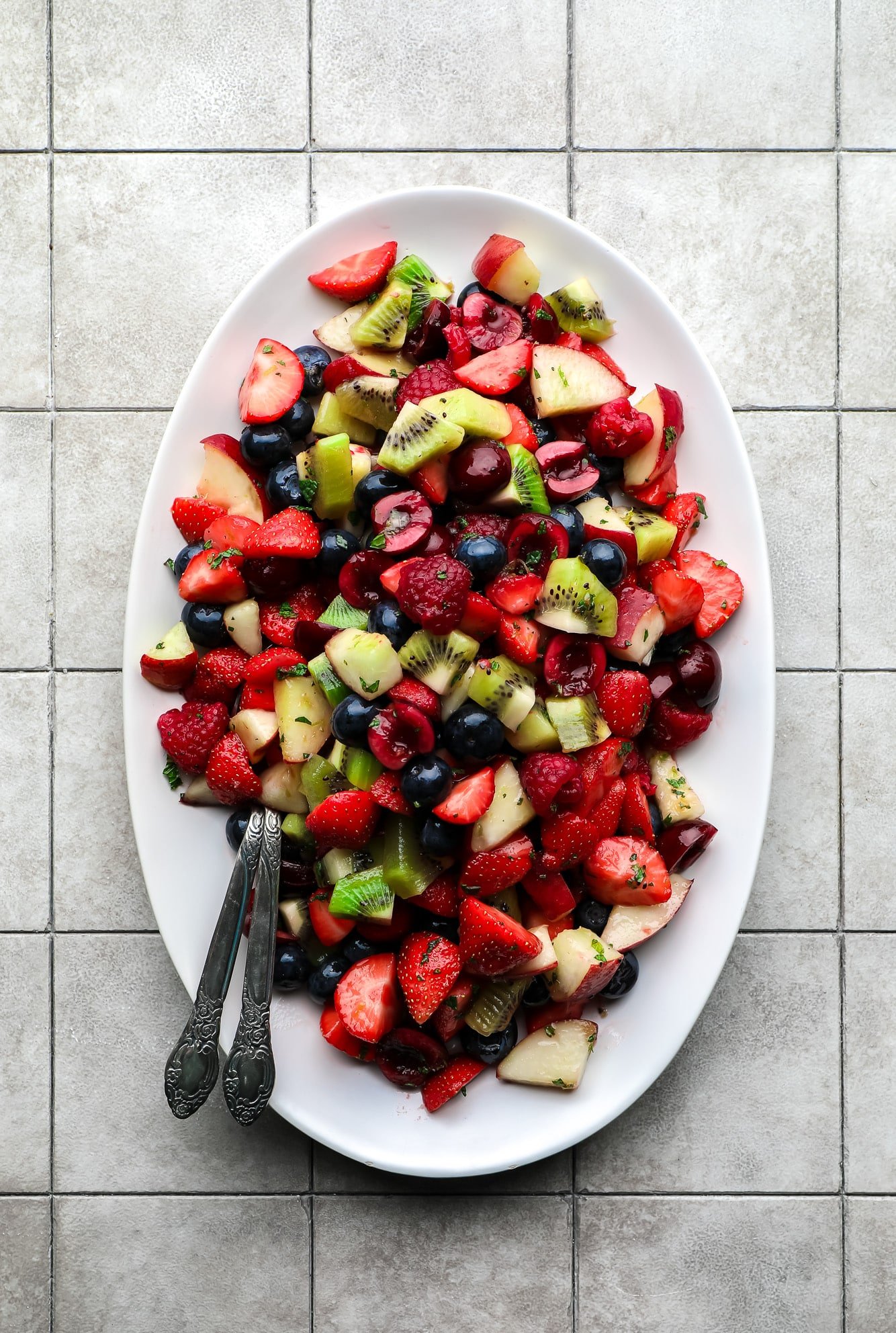 Fruit salad on a white portion dish with two spoons.
