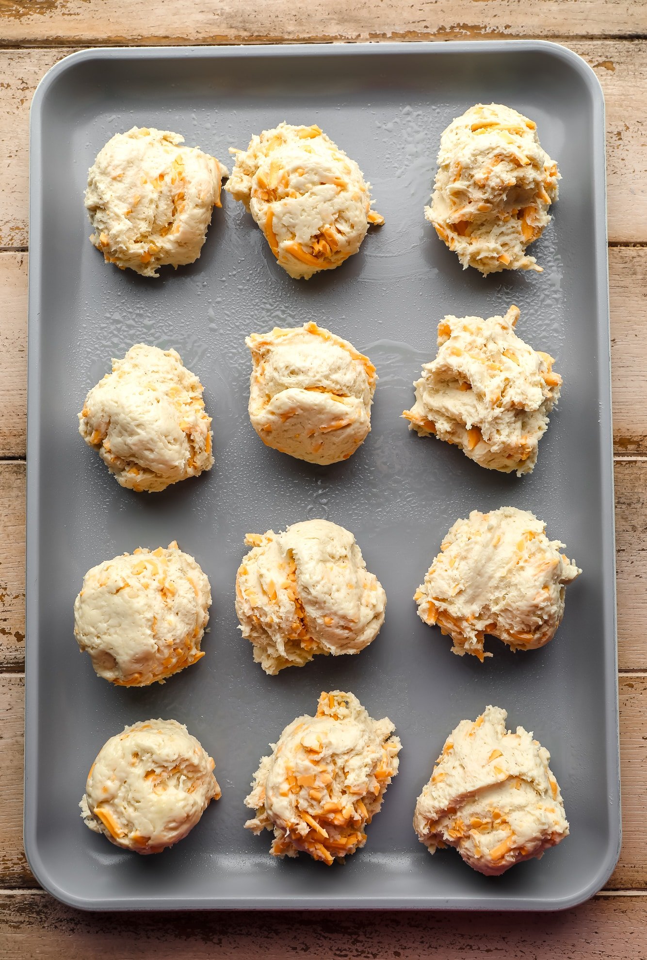 Scoops of Raw Vegan Cheddar Bady Biscuit Dough on a metal oven leaf.