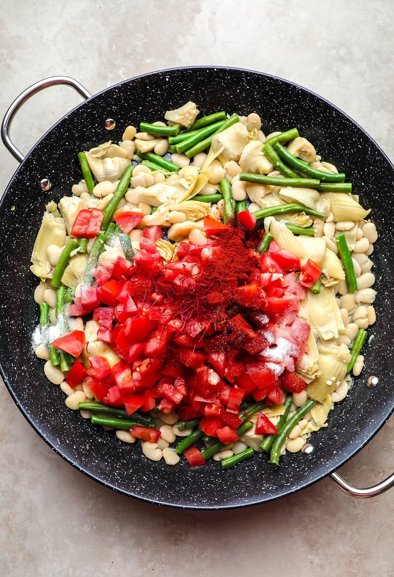 Chopped tomatoes and saffron on top of beans and artichoke hearts in a black paella.