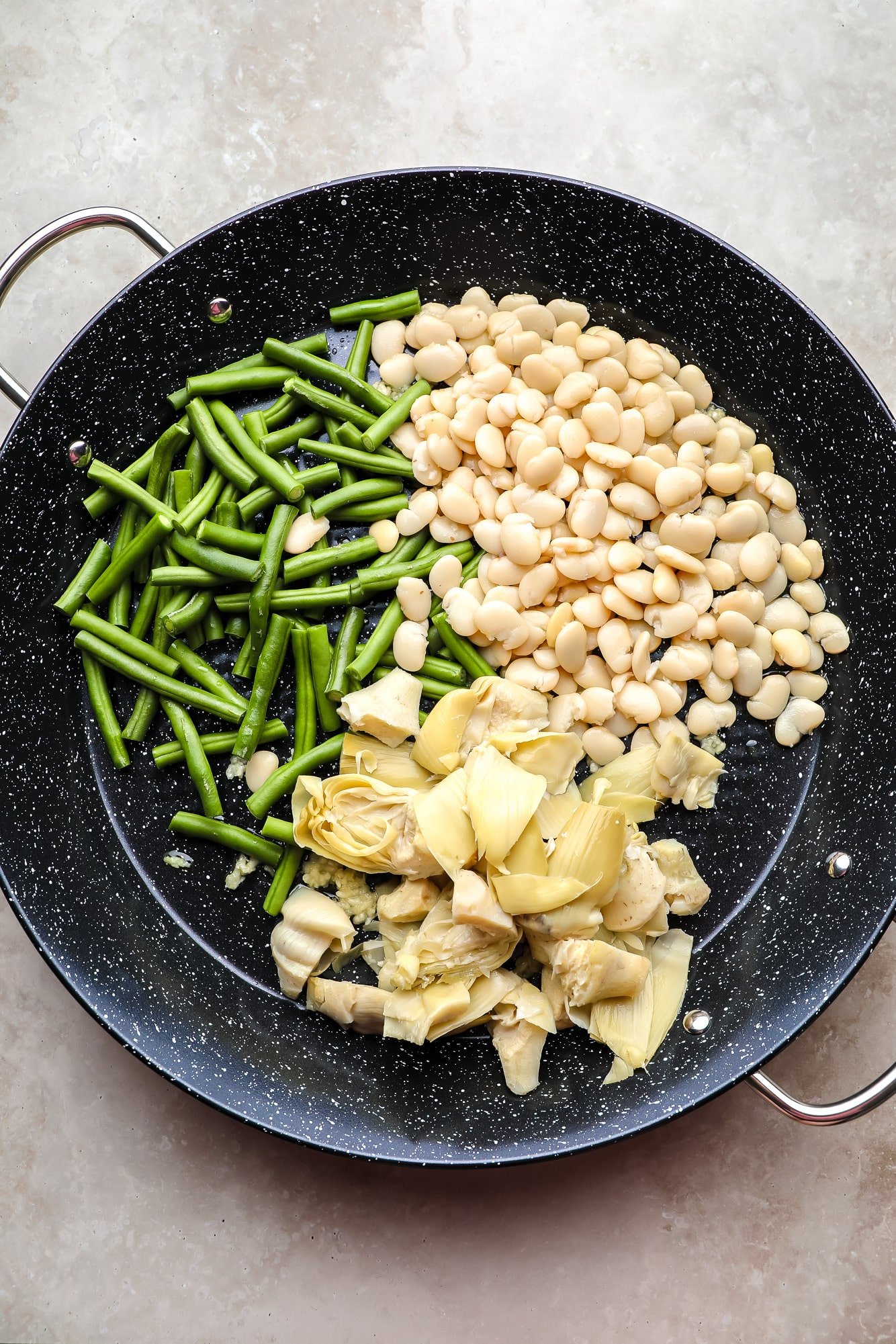 Green beans, artichoke hearts and white beans in a large pan of black paella.