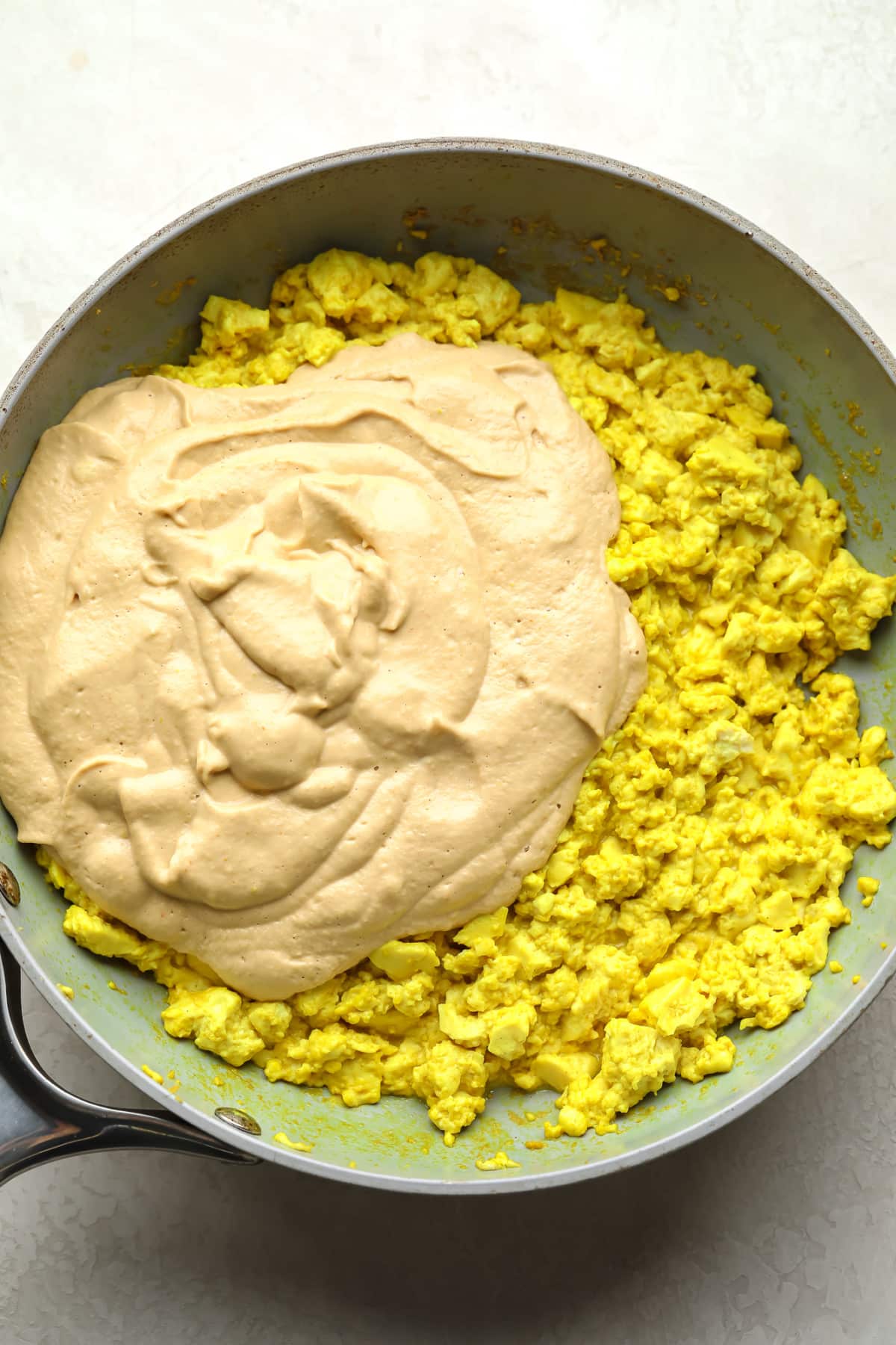 Yellow scramble tofu with creamy sauce is added to a pan