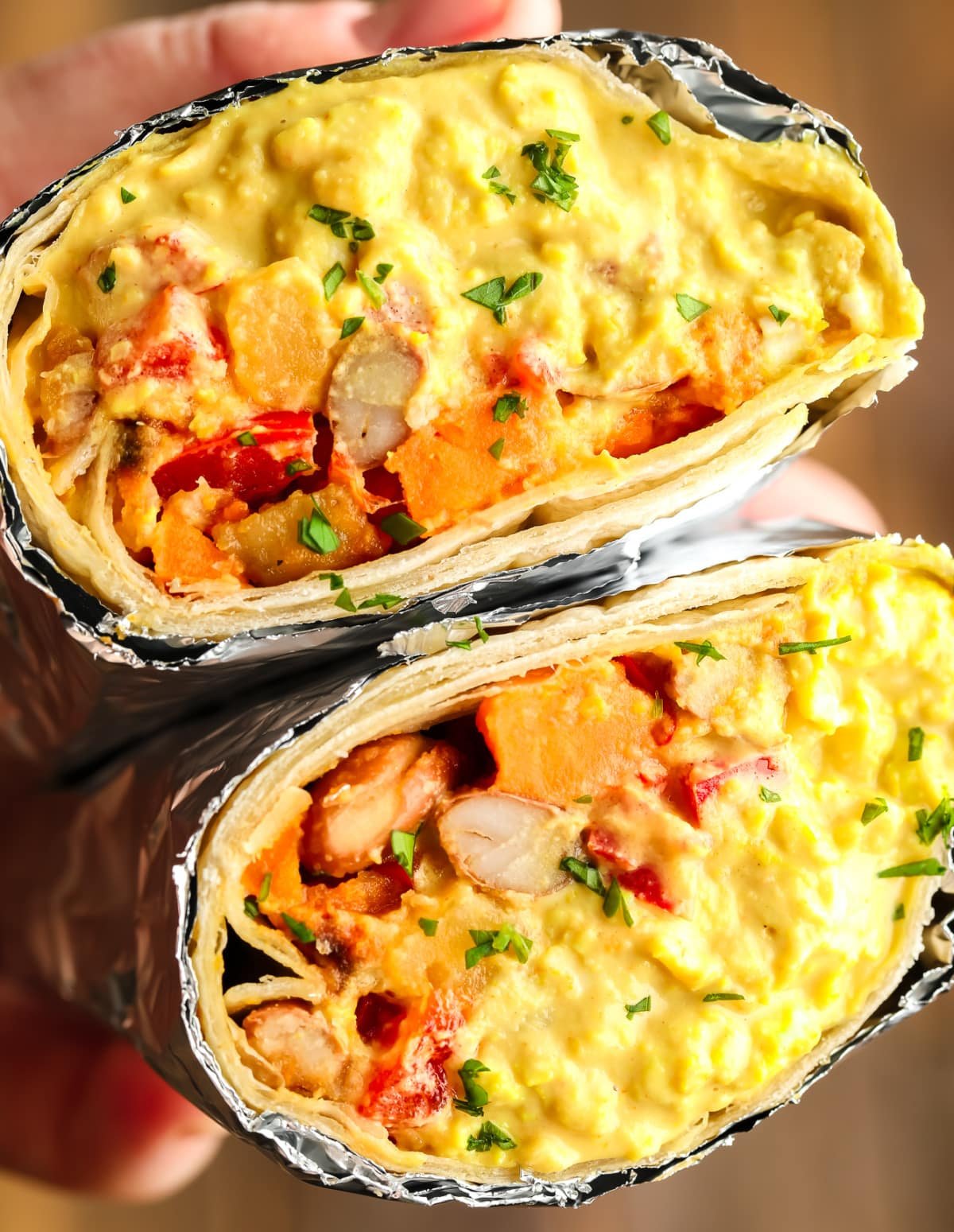 Eggy's yellow -looking mix in Vegan Breakfast Burrito, a hand that holds a cut in the middle of the Burrito