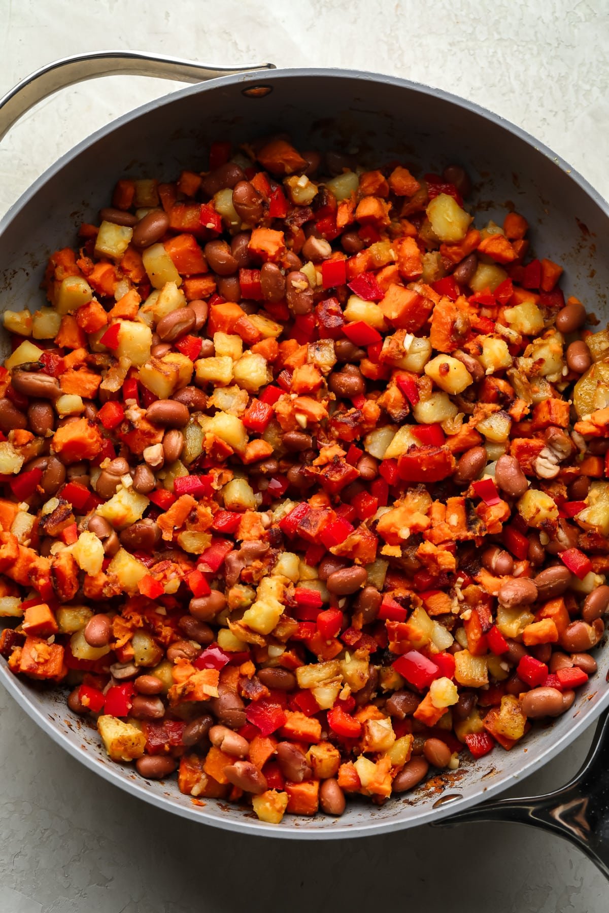 Hash breakfast in the pan with sweet and common potatoes, paprika and beans