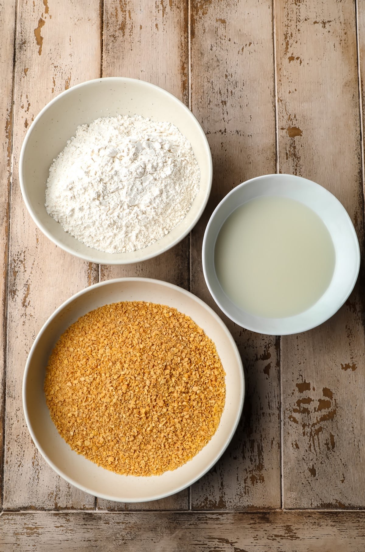 Bowl with breadcrumbs, flour and milk on wooden bottom