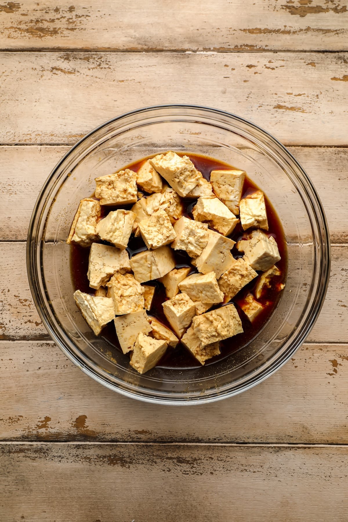 tofu pieces ripped in a glass bowl with marinated soy sauce on wooden bottom