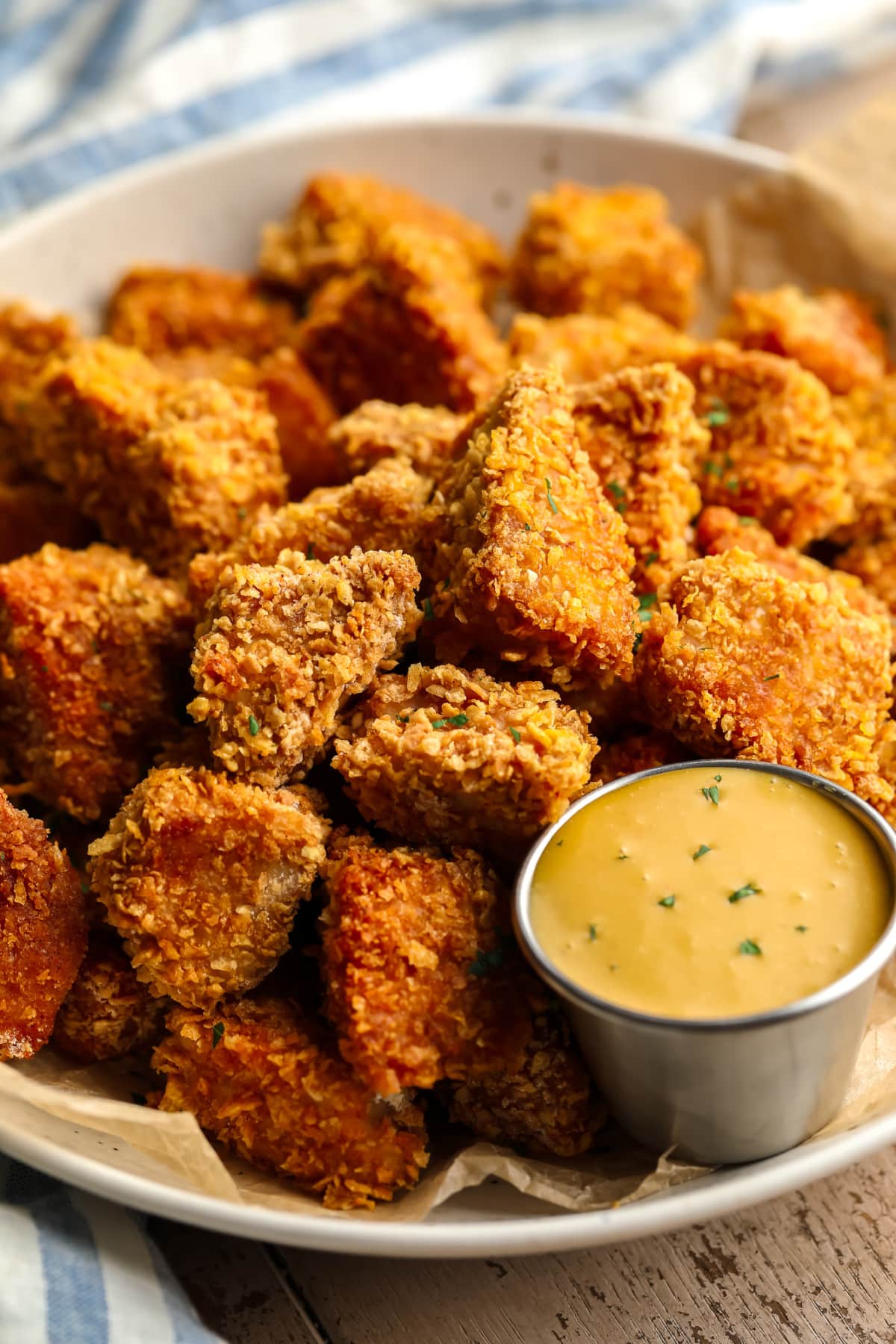 Nuggets of crunchy vegan chicken in a shallow bowl with yellow sauce, blue towel on the bottom