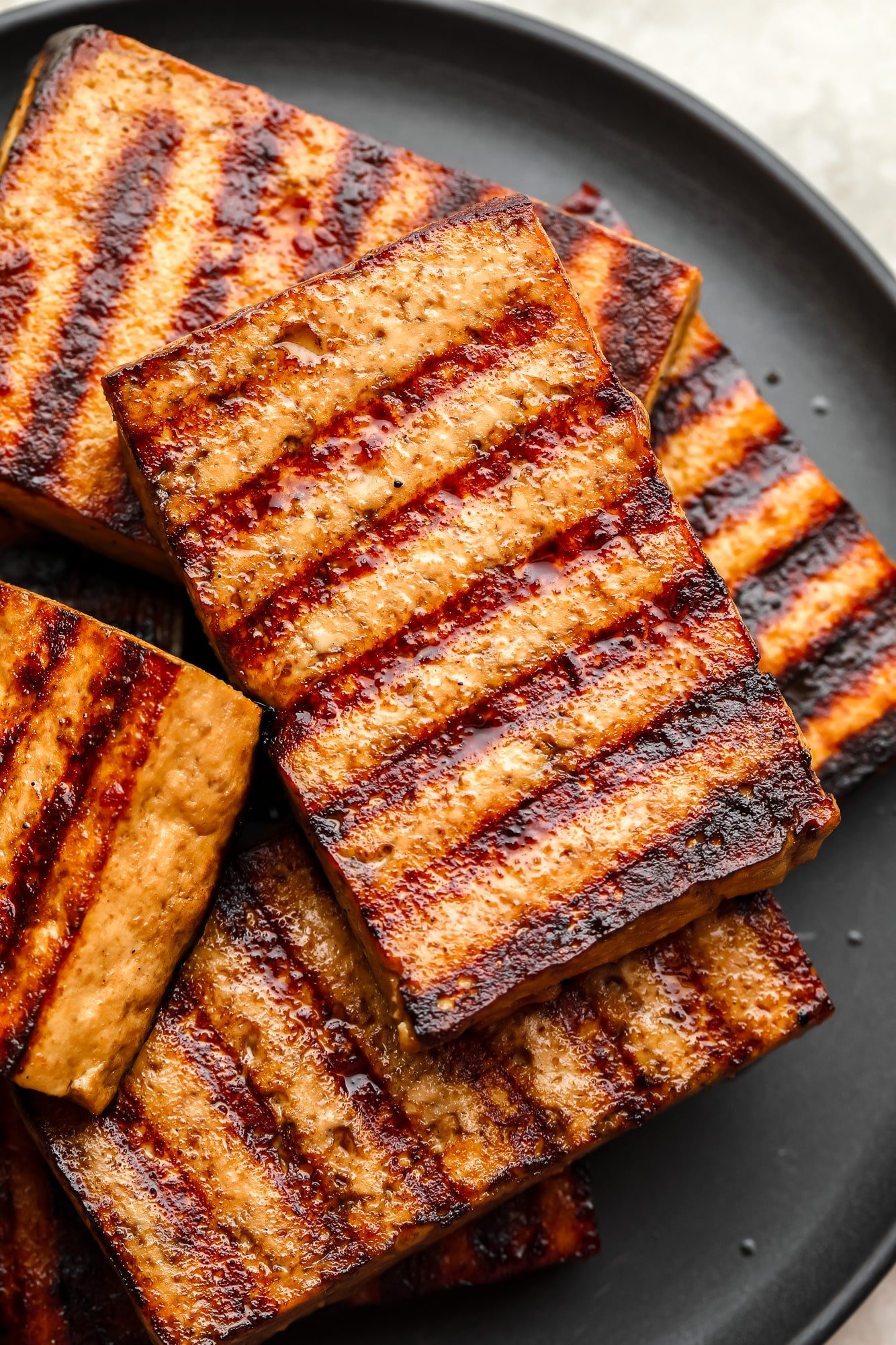 A pile of tofu pieces on the grill on a black dish.
