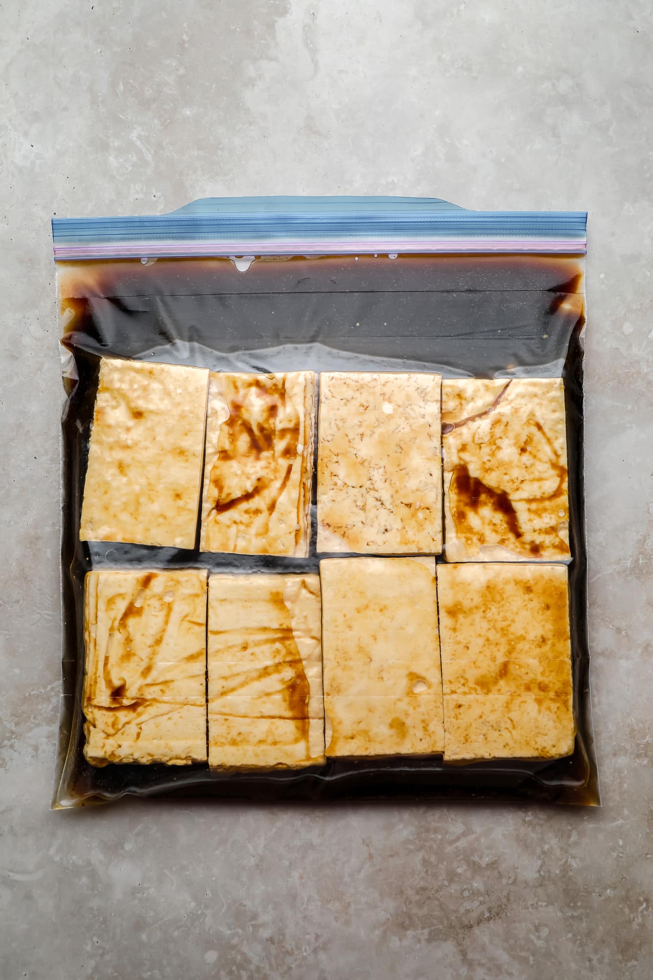 Rectangular tofu pieces and a marinade in a large bag.