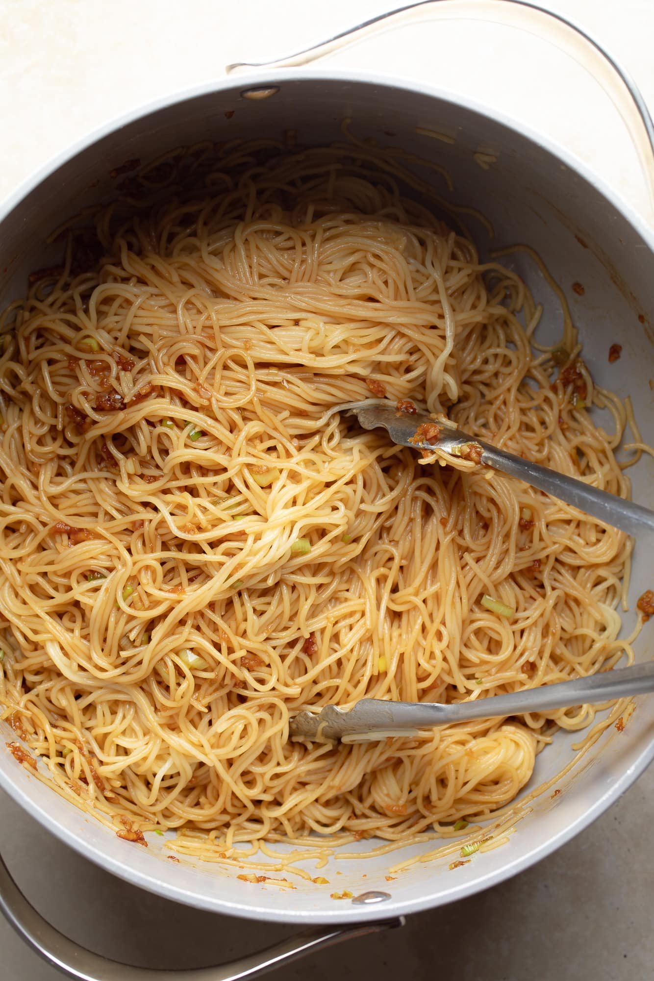 Using tongs to throw cooked noodles in garlic sauce.